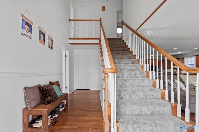 stairs with wood finished floors, a towering ceiling, and ornamental molding