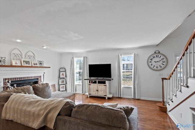living area with wood finished floors, stairway, a fireplace, and baseboards