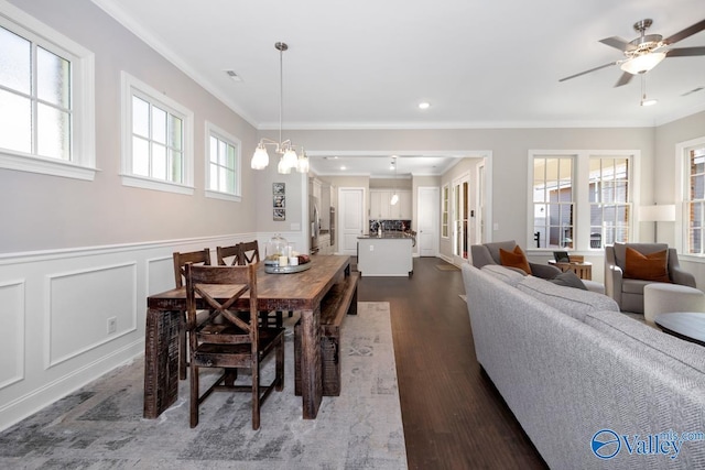 dining room featuring ceiling fan with notable chandelier, ornamental molding, dark wood-style flooring, and wainscoting