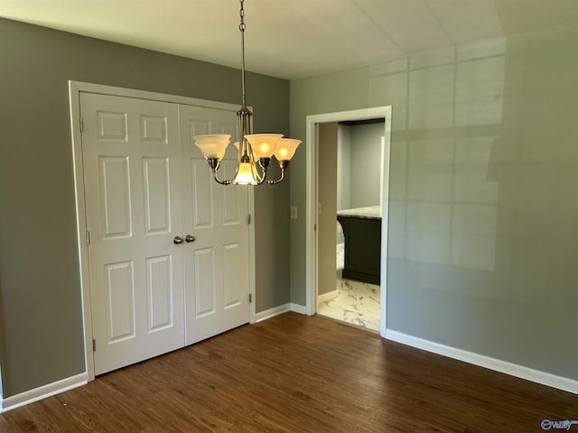 unfurnished bedroom with a notable chandelier, wood finished floors, and baseboards