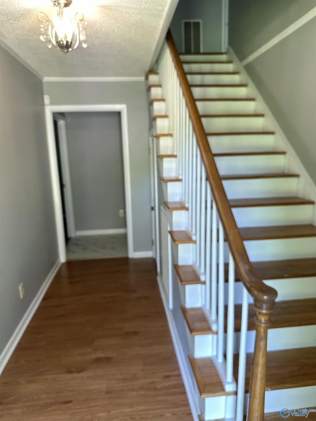 staircase with crown molding, an inviting chandelier, wood finished floors, and baseboards