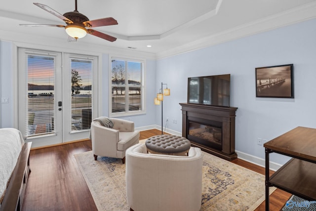 living room featuring ceiling fan, a tray ceiling, dark hardwood / wood-style floors, and ornamental molding