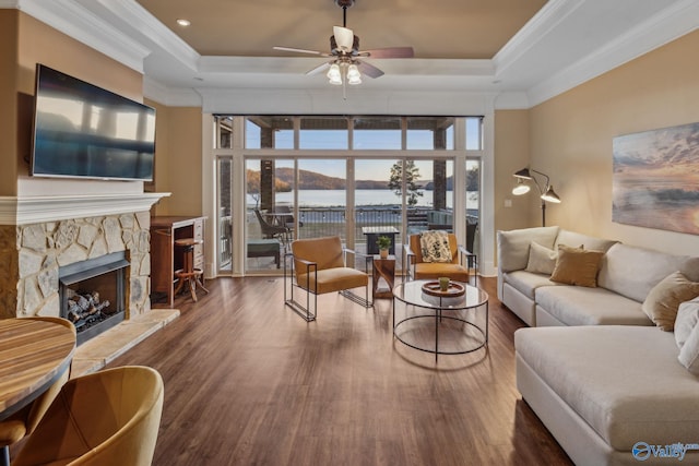 living room featuring a water view, a fireplace, a tray ceiling, and dark wood-type flooring