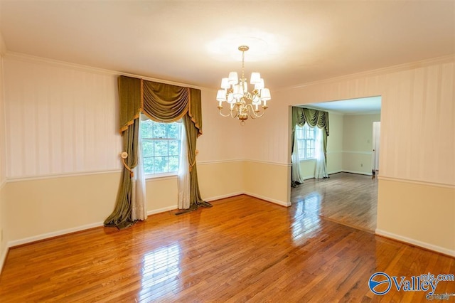 spare room with hardwood / wood-style flooring, an inviting chandelier, and crown molding