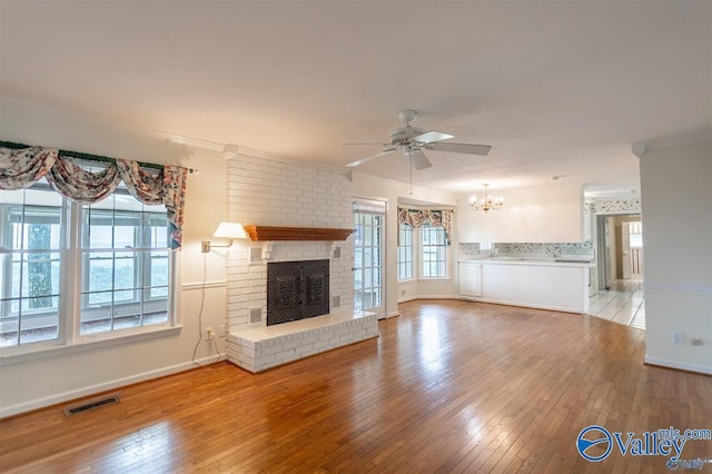 unfurnished living room with ceiling fan with notable chandelier, light hardwood / wood-style floors, ornamental molding, and a brick fireplace