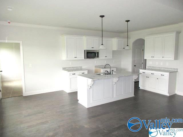 kitchen featuring hanging light fixtures, crown molding, a center island with sink, and white cabinets