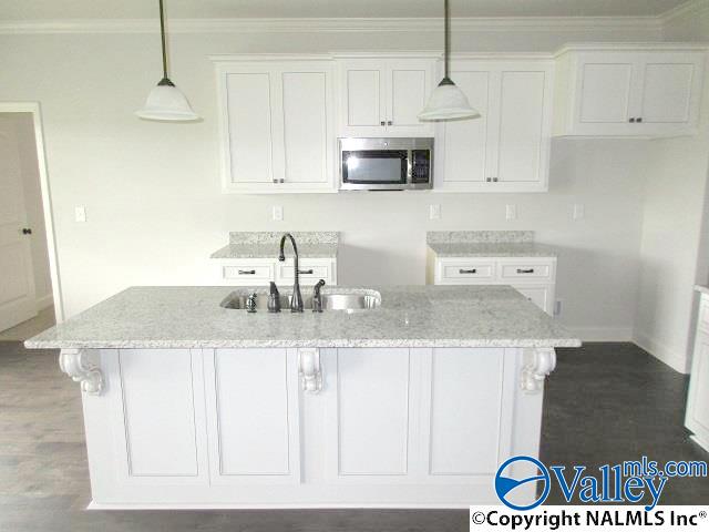 kitchen with an island with sink, sink, white cabinets, hanging light fixtures, and light stone counters