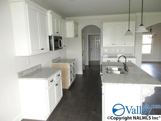 kitchen featuring white cabinetry, an island with sink, sink, hanging light fixtures, and light stone counters