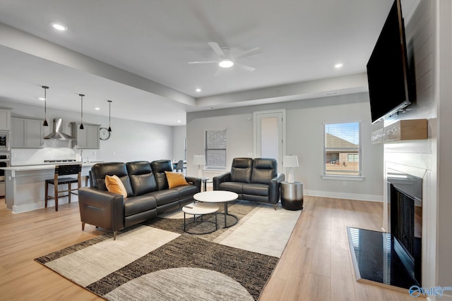 living room featuring ceiling fan, recessed lighting, a fireplace, baseboards, and light wood-style floors