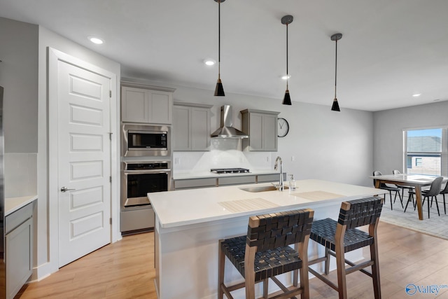 kitchen featuring wall chimney exhaust hood, appliances with stainless steel finishes, gray cabinets, light wood-type flooring, and a sink