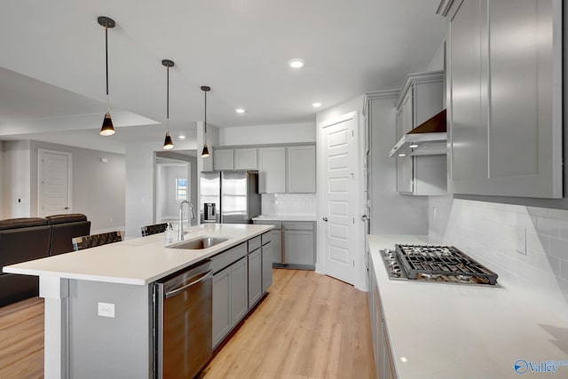 kitchen with open floor plan, stainless steel appliances, ventilation hood, gray cabinets, and a sink