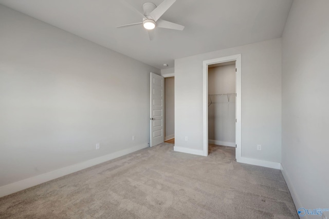 unfurnished bedroom featuring a walk in closet, a closet, a ceiling fan, light carpet, and baseboards