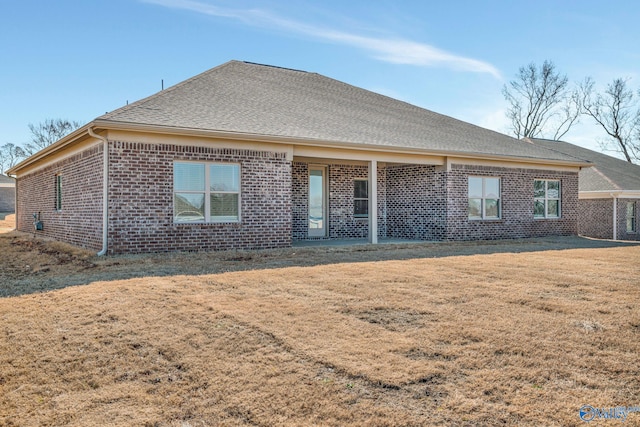 back of property with brick siding, roof with shingles, and a lawn