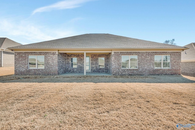 back of house with roof with shingles, brick siding, a lawn, and a patio