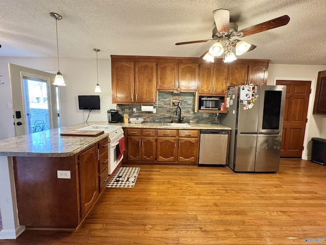 kitchen with sink, decorative backsplash, hanging light fixtures, kitchen peninsula, and stainless steel appliances