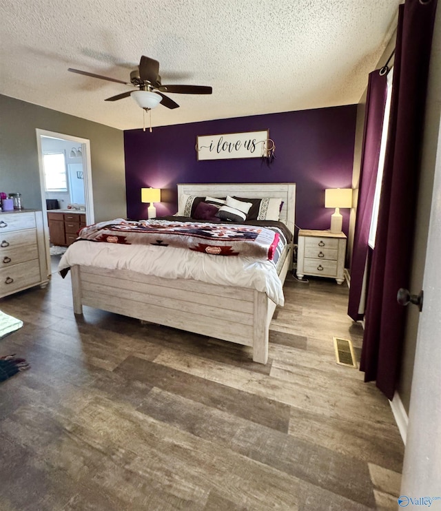 bedroom with ceiling fan, ensuite bathroom, dark hardwood / wood-style flooring, and a textured ceiling