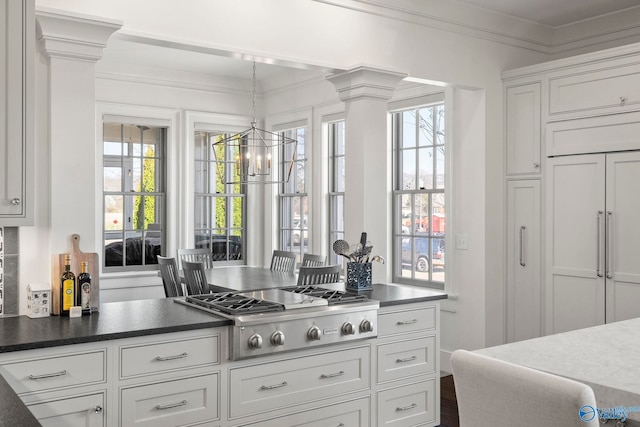 kitchen with a notable chandelier, ornamental molding, decorative columns, paneled built in refrigerator, and stainless steel gas cooktop