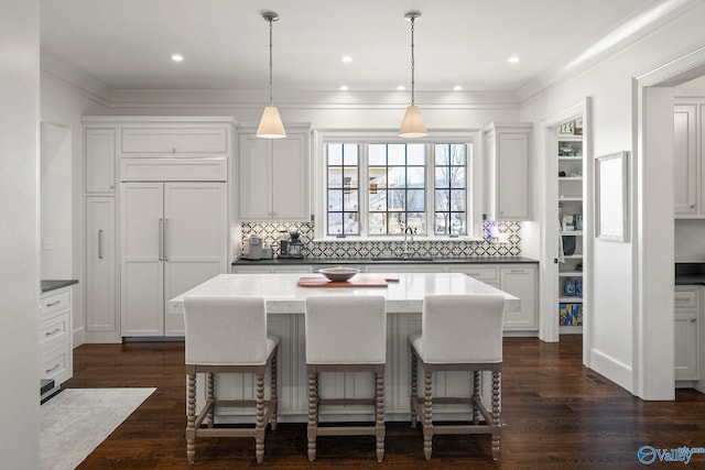 kitchen with ornamental molding, a kitchen island, paneled refrigerator, and dark wood-style flooring