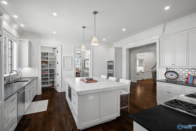 kitchen featuring a sink, dark wood-style floors, a center island, stainless steel appliances, and crown molding