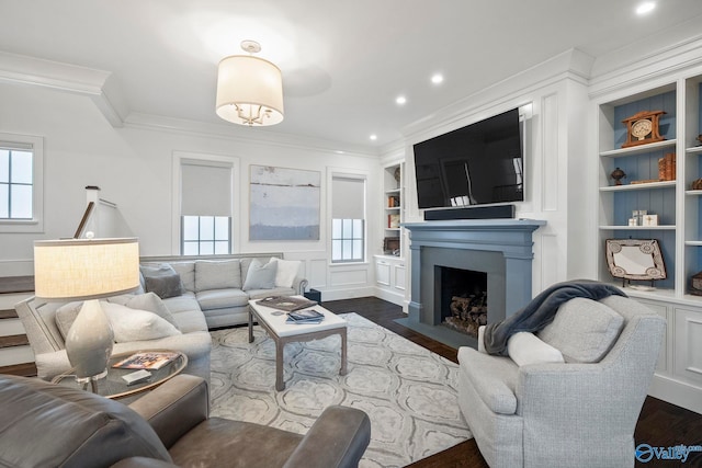 living area featuring a fireplace with flush hearth, built in shelves, recessed lighting, crown molding, and dark wood-style flooring