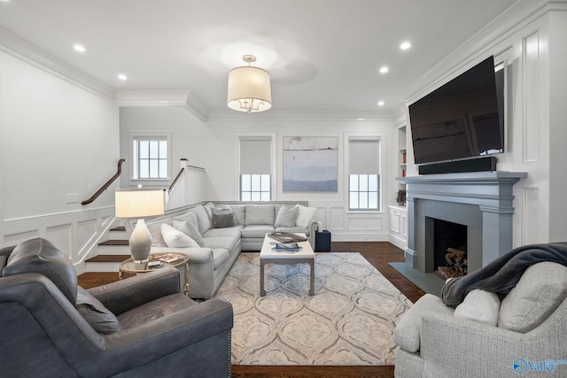 living area featuring a decorative wall, a fireplace with flush hearth, crown molding, and dark wood-type flooring