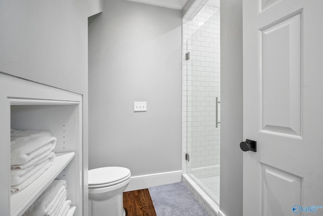 bathroom with toilet, wood finished floors, a stall shower, and baseboards