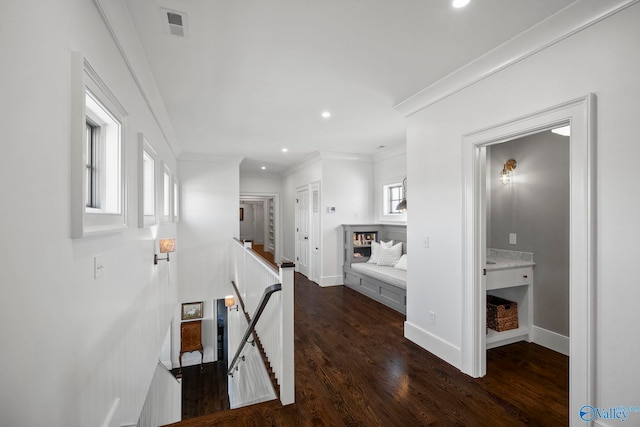 hallway with dark wood-style floors, visible vents, baseboards, crown molding, and an upstairs landing