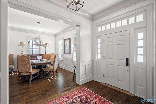 foyer featuring a wainscoted wall, dark wood-type flooring, a notable chandelier, and crown molding