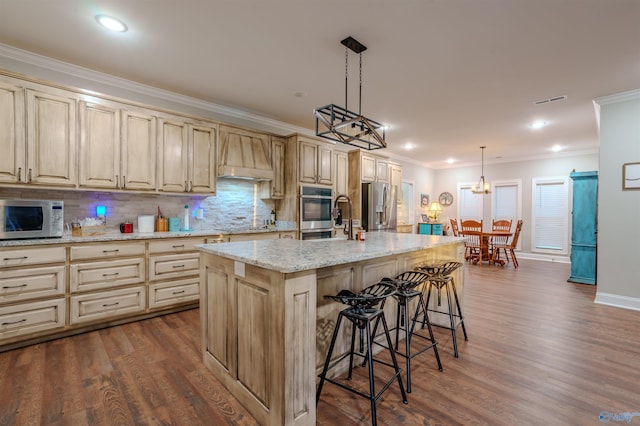 kitchen with decorative light fixtures, a kitchen bar, stainless steel appliances, crown molding, and a center island with sink