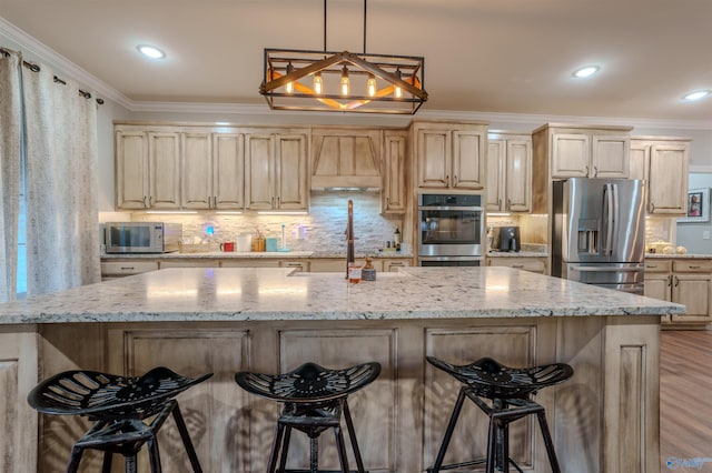 kitchen featuring appliances with stainless steel finishes, decorative light fixtures, ornamental molding, custom range hood, and a center island with sink