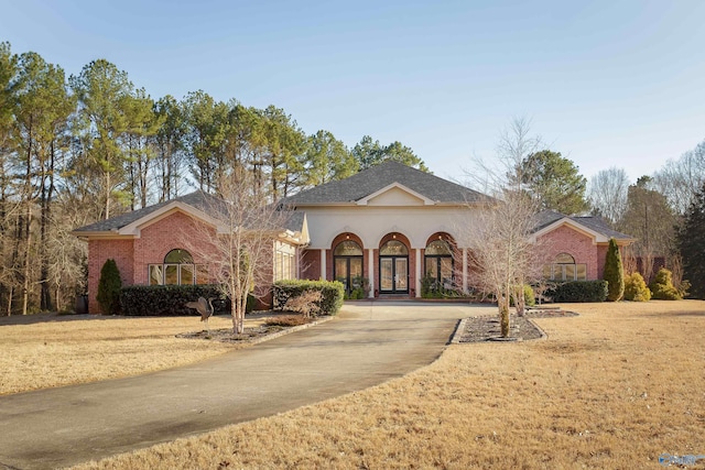 view of front facade featuring french doors, brick siding, driveway, and a front lawn