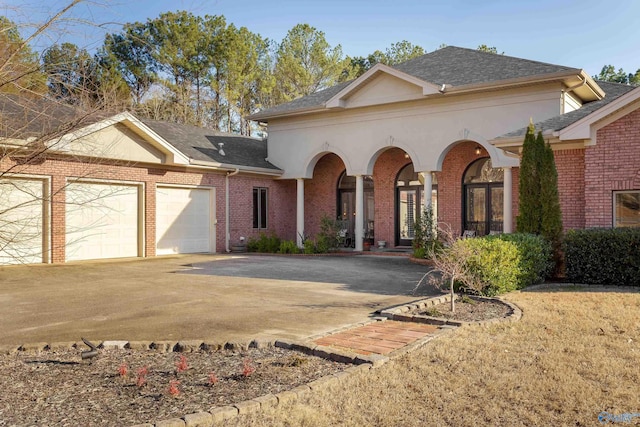 view of front of house with driveway, a shingled roof, a garage, and brick siding