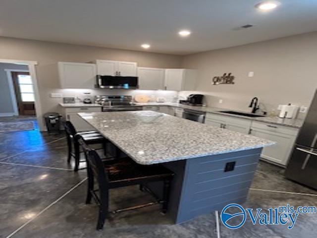 kitchen with sink, white cabinetry, a center island, appliances with stainless steel finishes, and a kitchen breakfast bar