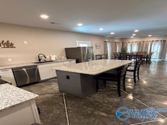 kitchen with white cabinetry, stainless steel appliances, a center island, and light stone counters