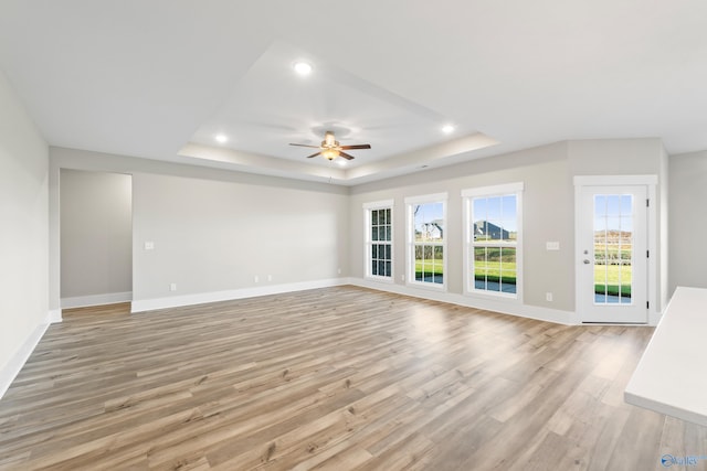 unfurnished living room featuring baseboards, light wood-type flooring, a raised ceiling, and a ceiling fan