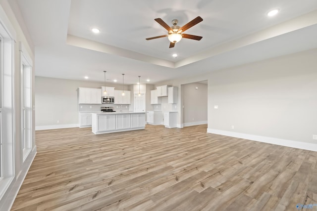 unfurnished living room with a raised ceiling, baseboards, light wood-type flooring, recessed lighting, and a ceiling fan