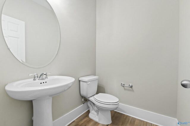 half bathroom with a sink, wood finished floors, toilet, and baseboards