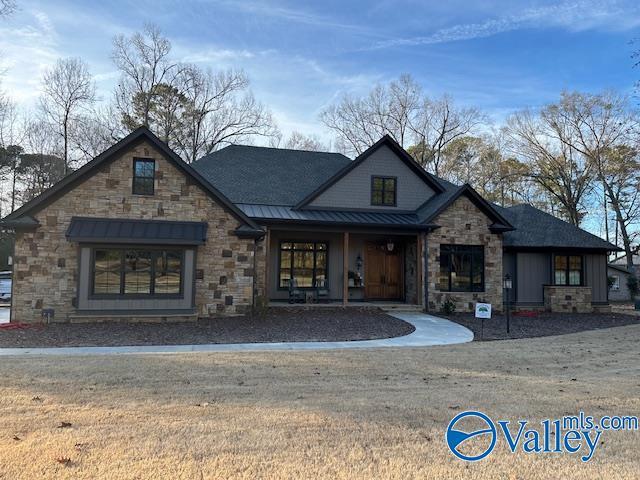 view of front of house with metal roof, covered porch, stone siding, a front lawn, and a standing seam roof