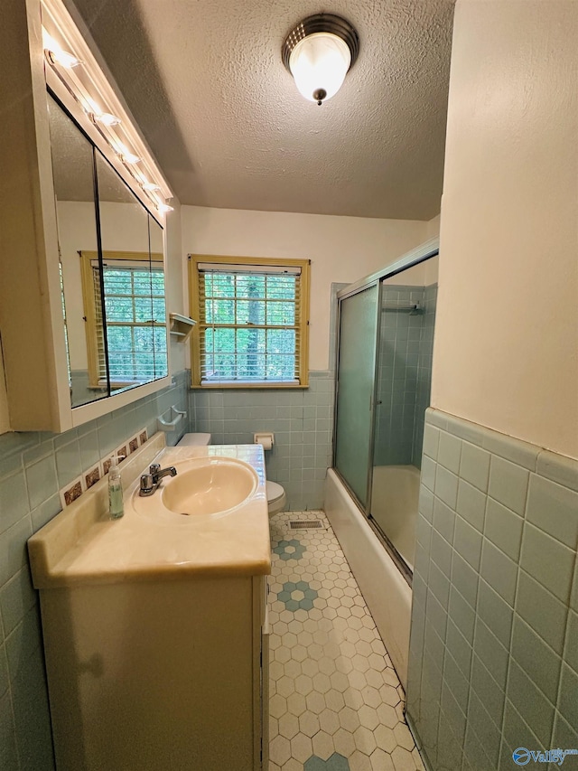 full bathroom with a textured ceiling, tile walls, tile patterned flooring, a wainscoted wall, and vanity