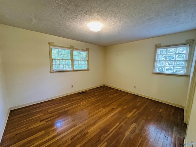 empty room featuring baseboards, a textured ceiling, and dark wood-style floors