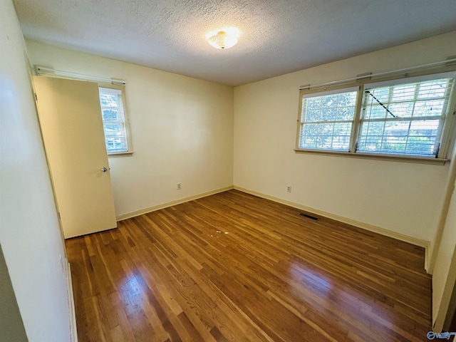 unfurnished room featuring baseboards, a textured ceiling, wood finished floors, and a healthy amount of sunlight