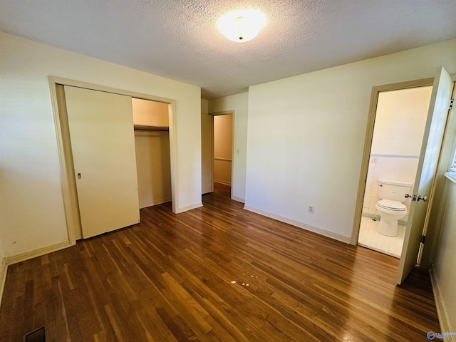 unfurnished bedroom featuring a textured ceiling, dark wood finished floors, baseboards, a closet, and ensuite bathroom