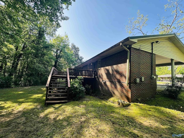view of side of home featuring stairs, a lawn, brick siding, and a deck