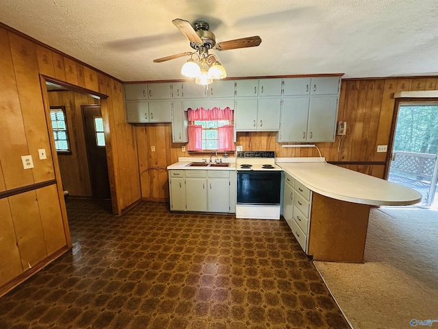 kitchen with electric range, a peninsula, wooden walls, light countertops, and a ceiling fan