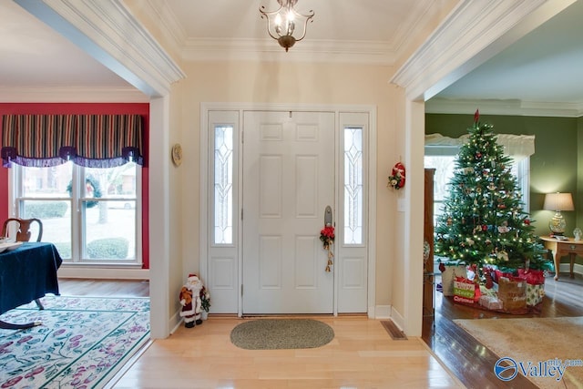 foyer entrance featuring an inviting chandelier, ornamental molding, and light wood-type flooring