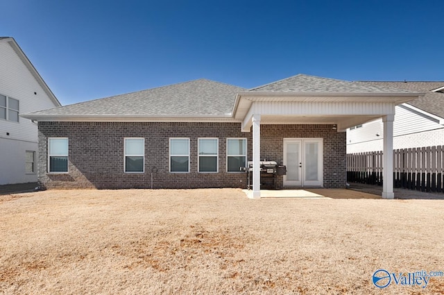 rear view of house with french doors, brick siding, fence, and roof with shingles