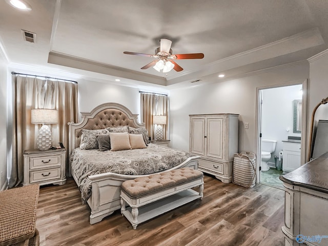 bedroom featuring a raised ceiling, ceiling fan, ornamental molding, ensuite bathroom, and dark wood-type flooring