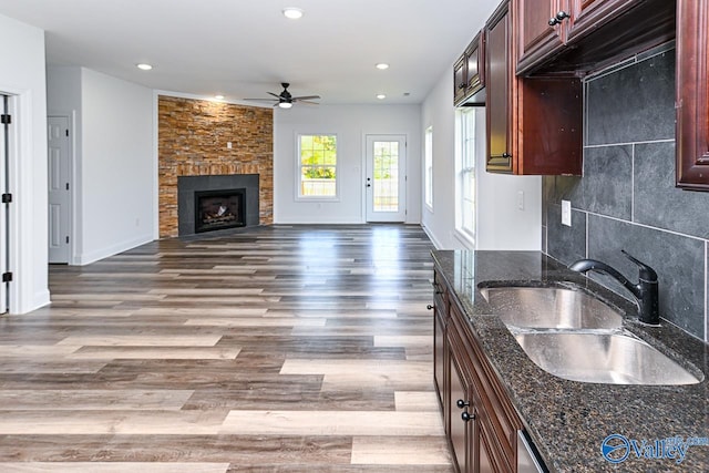 kitchen with dark stone counters, ceiling fan, sink, a fireplace, and hardwood / wood-style floors