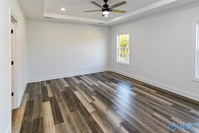 empty room with ceiling fan, a raised ceiling, and dark hardwood / wood-style flooring