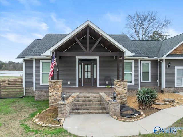 view of front of property featuring brick siding, fence, covered porch, and roof with shingles